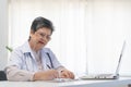 Senior asian physician, general woman doctor wearing glasses and white uniform, mature female with stethoscope, working on laptop Royalty Free Stock Photo