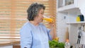 Senior asian woman drinking orange juice while standing by window in kitchen background, Old people retirement and healthy Royalty Free Stock Photo