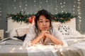 Senior asian woman relax on bed looking at xmas lights, attractive elderly sad lady in bedroom at home at christmas