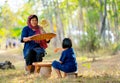 Senior Asian woman with traditional clothes winnow rice using basketry and little girl stay beside and also work with rice