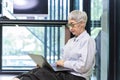 Senior Asian woman working online using laptop computer sitting in modern workplace for active old people and education concept Royalty Free Stock Photo