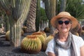 A senior attractive woman with straw hat sitting in the garden with cactus plants around her