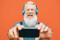 Senior bearded man making selfie with mobile phone while listening to his favorite playlist with headphones Royalty Free Stock Photo