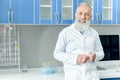 Senior bearded scientist in white coat holding tube with reagent in chemical laboratory