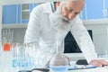 Senior bearded scientist in white coat writing in clipboard on tanle with flasks in chemical laboratory Royalty Free Stock Photo