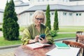 Senior beautiful business woman sitting on a chair and making notes in a notebook, with a phone and laptop in the yard Royalty Free Stock Photo