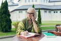 Senior beautiful business woman sitting on a chair and making notes in a notebook, with a phone and laptop in the yard Royalty Free Stock Photo