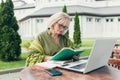 Senior beautiful business woman sitting on a chair and making notes in a notebook, with a phone and laptop in the yard Royalty Free Stock Photo