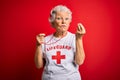 Senior beautiful grey-haired lifeguard woman wearing t-shirt with red cross using whistle Doing Italian gesture with hand and