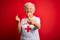 Senior beautiful grey-haired lifeguard woman wearing t-shirt with red cross using whistle pointing fingers to camera with happy