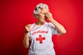 Senior beautiful grey-haired lifeguard woman wearing t-shirt with red cross using whistle tired rubbing nose and eyes feeling