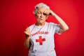 Senior beautiful grey-haired lifeguard woman wearing t-shirt with red cross using whistle worried and stressed about a problem