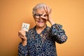 Senior beautiful grey-haired woman holding reminder paper with sad emotion face with happy face smiling doing ok sign with hand on Royalty Free Stock Photo