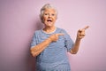 Senior beautiful grey-haired woman wearing casual t-shirt over isolated pink background smiling and looking at the camera pointing Royalty Free Stock Photo