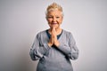 Senior beautiful grey-haired woman wearing golden queen crown over white background praying with hands together asking for