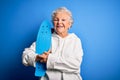 Senior beautiful sporty woman holding skate standing over isolated blue background with a happy face standing and smiling with a Royalty Free Stock Photo