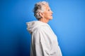 Senior beautiful sporty woman wearing white sweatshirt over isolated blue background looking to side, relax profile pose with Royalty Free Stock Photo