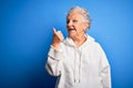 Senior beautiful sporty woman wearing white sweatshirt over isolated blue background smiling with happy face looking and pointing Royalty Free Stock Photo