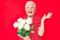 Senior beautiful woman with blue eyes and grey hair holding bouquet of white flowers celebrating victory with happy smile and Royalty Free Stock Photo