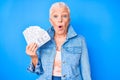 Senior beautiful woman with blue eyes and grey hair holding dollars scared and amazed with open mouth for surprise, disbelief face Royalty Free Stock Photo