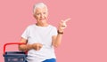 Senior beautiful woman with blue eyes and grey hair holding supermarket shopping basket smiling happy pointing with hand and Royalty Free Stock Photo