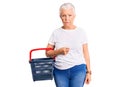 Senior beautiful woman with blue eyes and grey hair holding supermarket shopping basket thinking attitude and sober expression Royalty Free Stock Photo