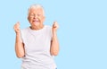 Senior beautiful woman with blue eyes and grey hair wearing casual white tshirt excited for success with arms raised and eyes Royalty Free Stock Photo