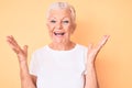 Senior beautiful woman with blue eyes and grey hair wearing classic white tshirt over yellow background celebrating crazy and Royalty Free Stock Photo