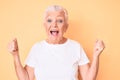 Senior beautiful woman with blue eyes and grey hair wearing classic white tshirt over yellow background celebrating surprised and Royalty Free Stock Photo