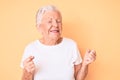 Senior beautiful woman with blue eyes and grey hair wearing classic white tshirt over yellow background excited for success with Royalty Free Stock Photo