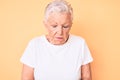 Senior beautiful woman with blue eyes and grey hair wearing classic white tshirt over yellow background with hand on stomach Royalty Free Stock Photo