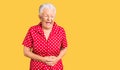 Senior beautiful woman with blue eyes and grey hair wearing a red summer dress with hand on stomach because nausea, painful Royalty Free Stock Photo