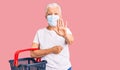 Senior beautiful woman with blue eyes and grey hair wearing shopping basket and medical mask with open hand doing stop sign with Royalty Free Stock Photo