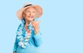 Senior beautiful woman with blue eyes and grey hair wearing summer hat and hawaiian lei smiling with happy face looking and Royalty Free Stock Photo