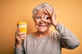 Senior beautiful woman drinking cup of coffee standing over isolated yellow background with happy face smiling doing ok sign with Royalty Free Stock Photo