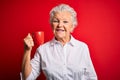 Senior beautiful woman drinking mug of coffee standing over isolated red background with a happy face standing and smiling with a Royalty Free Stock Photo