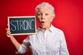 Senior beautiful woman holding blackboard with strong message over isolated red background scared in shock with a surprise face, Royalty Free Stock Photo