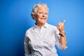 Senior beautiful woman wearing elegant shirt standing over isolated blue background smiling with happy face looking and pointing Royalty Free Stock Photo