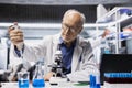 Senior biochemist in lab adding drops of liquid into blue solution Royalty Free Stock Photo
