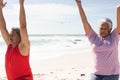 Senior biracial couple exercising together with arms raised at beach against sky on sunny day Royalty Free Stock Photo