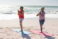 Senior biracial couple practicing tree pose yoga on exercise mats at beach during sunny day