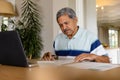 Senior biracial man doing paperwork and using laptop in dining room Royalty Free Stock Photo