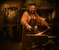 Senior blacksmith forging the molten metal on the anvil in smithy Royalty Free Stock Photo