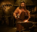 Senior blacksmith forging the molten metal on the anvil in smithy Royalty Free Stock Photo