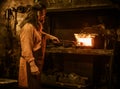 Senior blacksmith heats item before forging in smithy Royalty Free Stock Photo