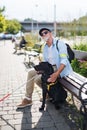 Senior blind man with guide dog sitting on bench in park in city. Royalty Free Stock Photo