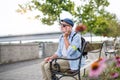 Senior blind man with smartphone sitting on bench in park in city. Royalty Free Stock Photo