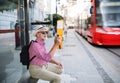 Senior blind man with white cane waiting for public transport in city.