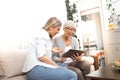 A senior blonde woman has a tablet in her hand while a young woman explains how to use the internet, social networks and online