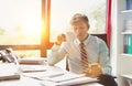 Senior business man drinking a coffee and checking smart phone  whilst sitting in his small real life office Royalty Free Stock Photo